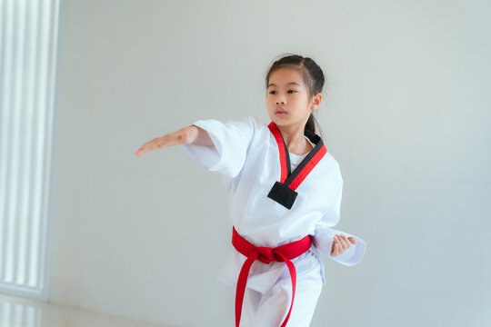 Young girl practices martial arts in a studio during a training session with a red belt and focused expression