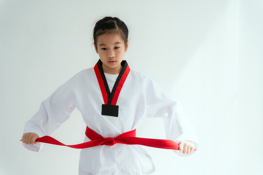Young girl ties red belt in martial arts uniform in a white room during training session