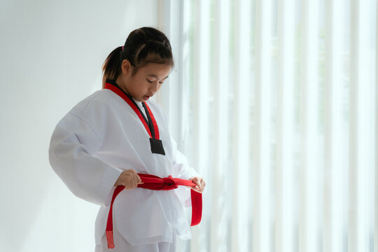 Young girl ties red belt in martial arts uniform in a white room during training session