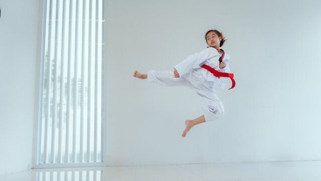 Child practices martial arts with a jump kick in a bright indoor space during training session