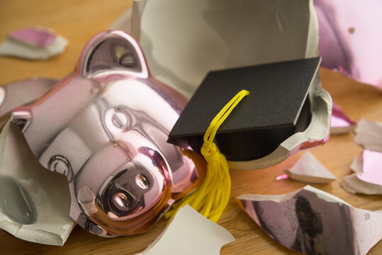 Close up mortarboard in broken piggy bank. Spending savings money for education, student loan or debt, paying tuition, personal financial problem crisis, social issue and so on concept.