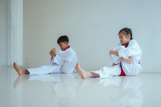 Young children practice stretching exercises in a bright room during a martial arts class in the afternoon