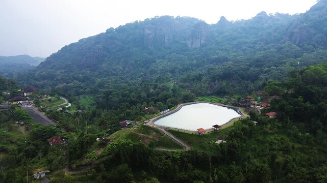 Aerial drone footage of Embung Nglanggeran, a scenic artificial reservoir located in the Ancient Nglanggeran Volcano area, Yogyakarta, Indonesia.