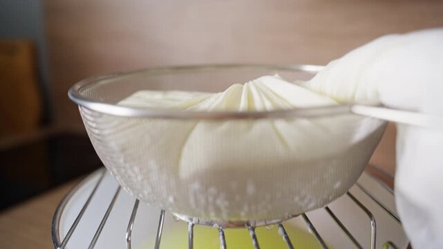 Homemade Cottage Cheese Draining Through Cheesecloth in a Metal Strainer Above a Bowl in a Kitchen. Traditional Dairy Making and Healthy Nutrition