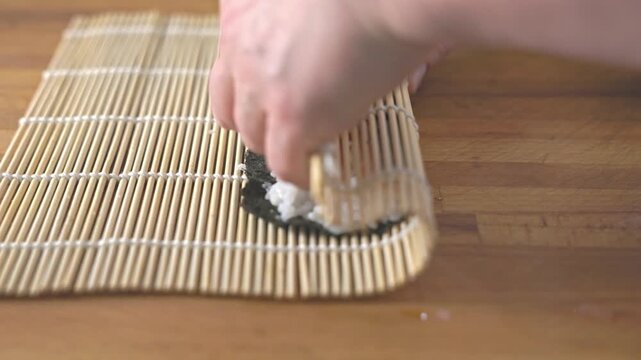 Close up of chef hands rolling homemade sushi with salmon and rice on bamboo mat.
