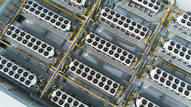 Close up aerial view of industrial HVAC ventilation fans and cooling units in symmetrical rows on a commercial rooftop.