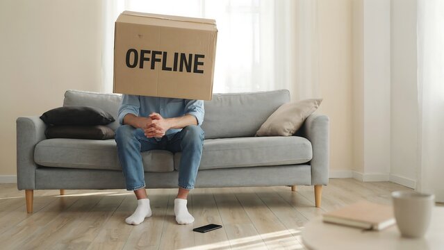 Man sitting on sofa holding offline sign in front of face representing digital disconnection and internet outage