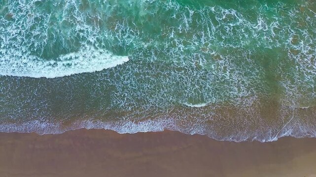 Aerial view of ocean waves crashing with white foam. Green water churns as waves meet the shore. Perfect for travel, adventure.