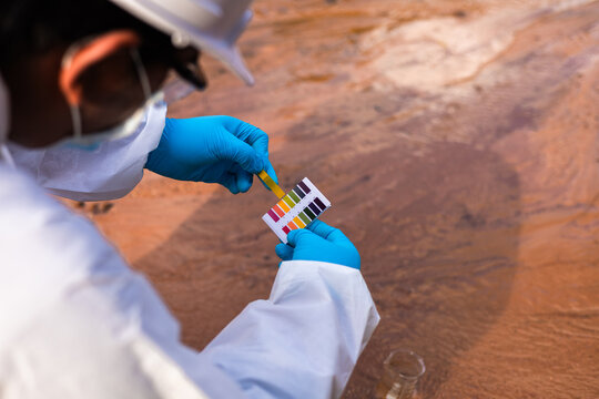 Researcher in protective gloves comparing litmus test paper color chart for acidity analysis.