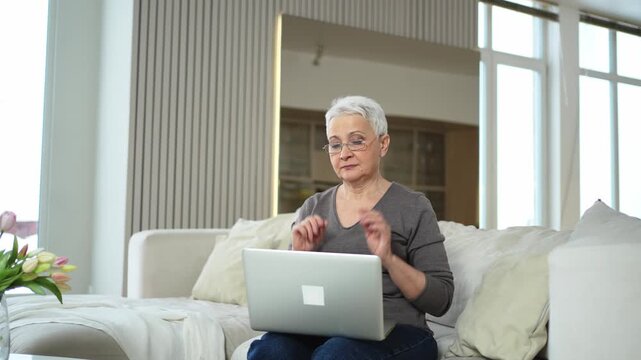 Middle aged senior woman at home relaxing stretching hands and body taking break from work on laptop. Older mature woman happy after work done satisfied by good result. Fatigue from long laptop usage
