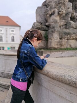 Girl using smartphone outdoors next to historical stone wall