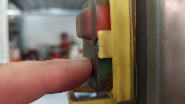 Close-up of a finger pressing the red stop button and green start button on industrial machinery