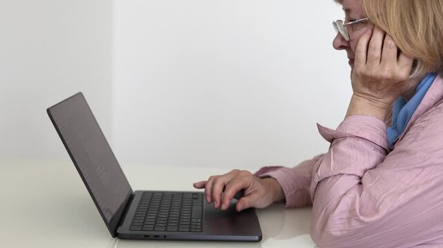 Senior woman sitting at home and using a laptop touchpad while reading information on the screen. Mature woman browsing the internet, working online or using digital services.