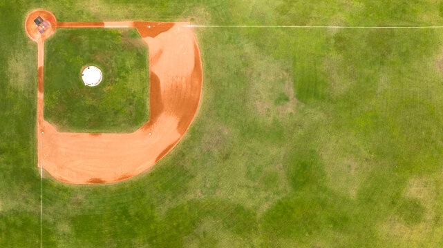 Zenithal aerial view of a baseball infield diamond, highlighting the contrasting textures between the smooth red clay running paths, the central green turf, and the clean pitcher's mound circle.