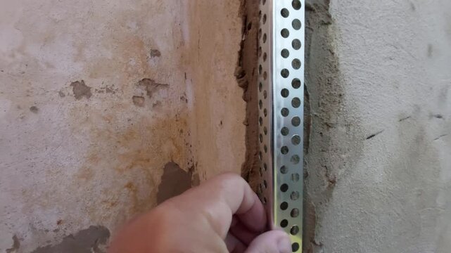 Construction worker installing a metal corner bead profile on an old plaster wall