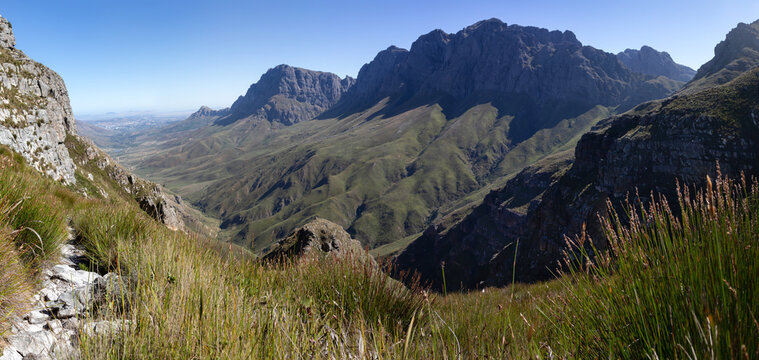 High resolution stitched panorama of Jonkershoek Nature Reserve, South Africa, featuring a rugged rocky hiking trail with a wide angle view of the majestic Twin Peaks mountain range and deep valley.