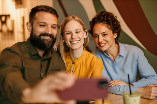 Friends taking happy group selfie with smartphone in cafe