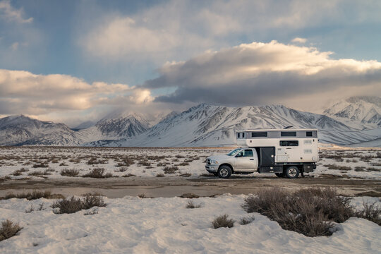 January 15, 2026-California, US- Truck camper recreational vehicle on a cross country roadtrip in winter parked in wilderness area with Sierra Nevada mountains and dramatic sky at sunset.