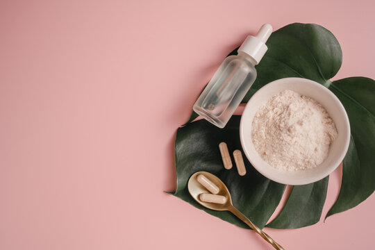 Collagen powder, capsules and serum bottle on monstera leaf over pink background