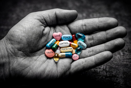 Hand holding colorful pills with conceptual words like love, peace, control and dreams