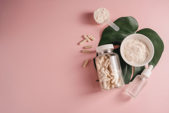 Collagen powder, food supplements capsules and serum bottle on monstera leaf over pink background