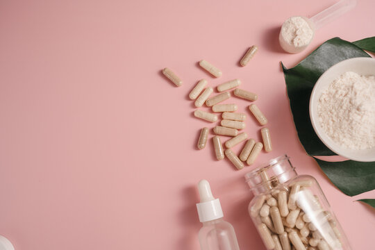 Collagen powder, food supplements capsules and serum bottle on monstera leaf over pink background