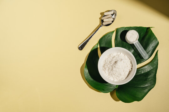 Collagen powder and supplement capsules with tropical leaves on yellow background, wellness concept