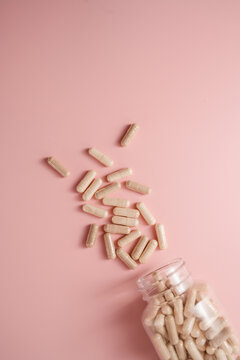 Collagen supplement capsules spilling from bottle on pink background with copy space, feminine food supplement abstract background