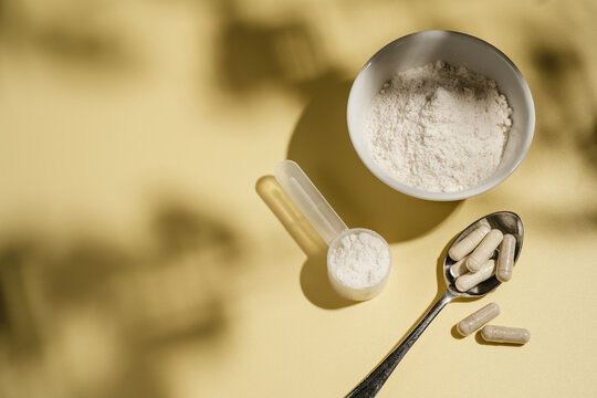 Collagen powder, capsules and scoop on yellow background with sun light and dark shadows, food supplement concept