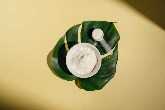 Collagen powder in a scoop, with tropical leaves on yellow background, wellness concept flat lay