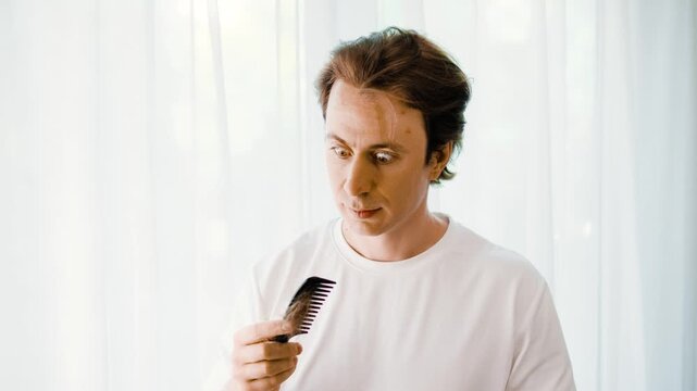 Shocked man discovers a large clump of hair loss while combing his hair. Concept of male alopecia, stress-related hair thinning, and grooming problems. High quality 4k footage