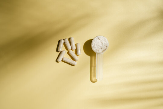 Collagen powder scoop and dietary supplement capsules on yellow background, flat lay with copy space