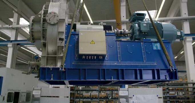Large industrial machine suspended by a crane in a manufacturing facility