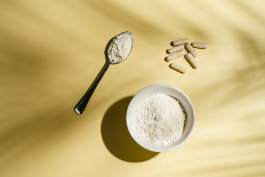 Collagen powder and dietary supplement capsules on yellow background with leaf shadows, flat lay