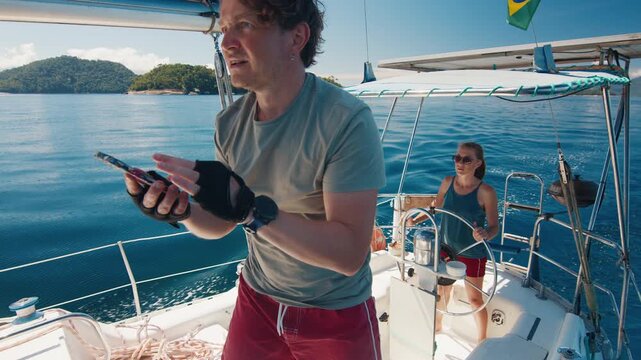 Sailing in the smooth sea during sunny day and navigate with the cellphone. Man and woman sail the small sailing boat in the region of the island of Ilha Grande in Brazil