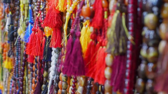 Close up of vibrant red, yellow, purple tassels with wooden beads hanging together at traditional market stall, showcasing rich textile craftsmanship, cultural merchandise.