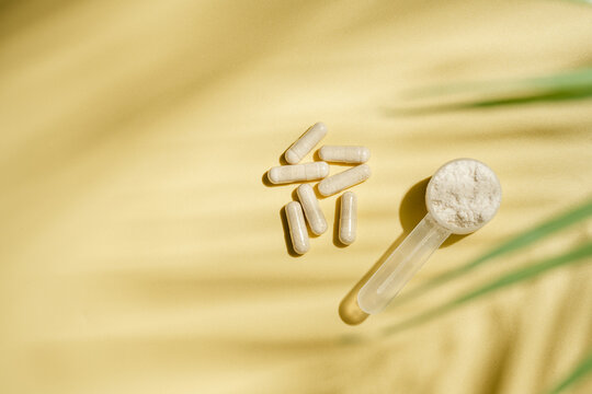 Collagen powder scoop and capsules on yellow background with copy space