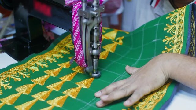 Close up of sewing machine needle stitching gold decorative embroidery on green textile with intricate traditional design pattern.