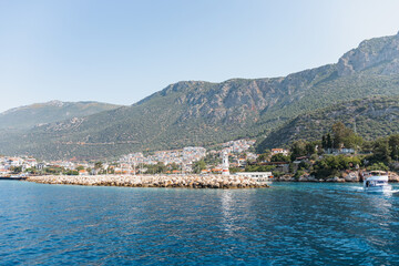 Fototapeta premium A scenic view of Kas, Turkey, featuring a rocky coastline, clear blue water, and green mountains in the background. Small boats are visible near the shore.