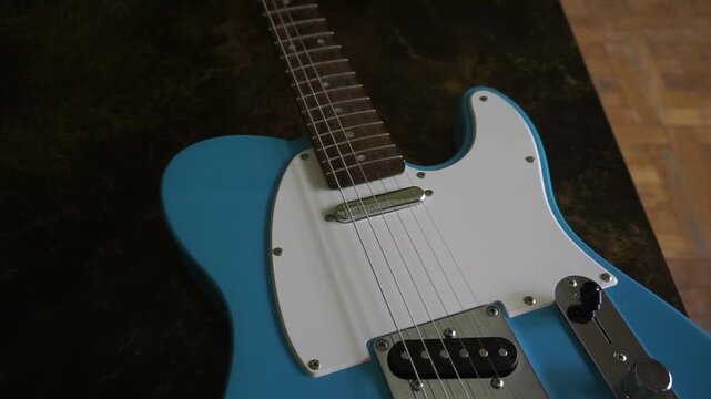Close-up of a light blue electric guitar body with strings, pickups, and fretboard
