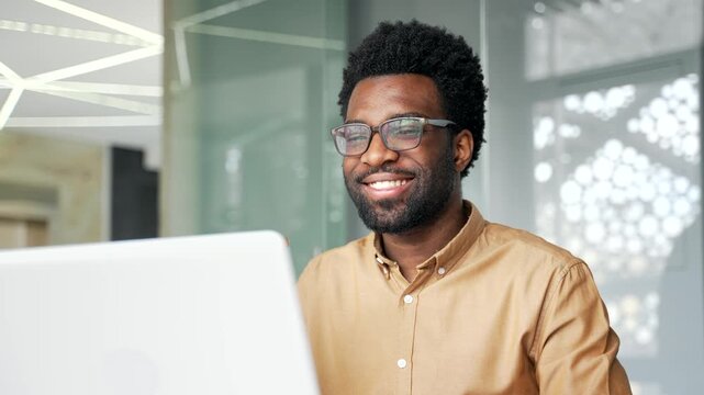Close up of smiling African American businessman in glasses reading good news on laptop screen. Satisfied black man manager looking at computer, gets positive email, feedback or successful report.