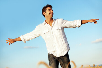Obraz premium Smile, blue sky and man in field with open arms, freedom and happiness for holiday or vacation. Countryside, nature and person with wellness, fresh air and thinking for break, weekend and travel
