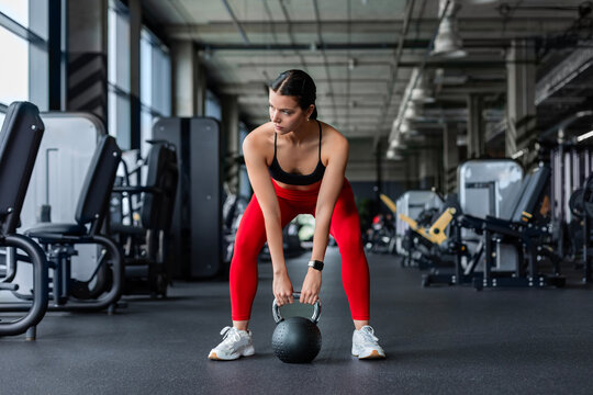Fit brunette female athlete in red leggings exercising with kettlebell