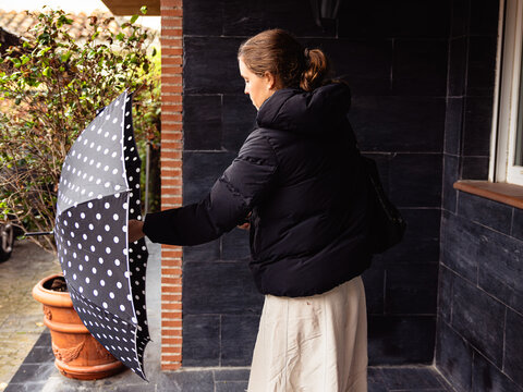 Woman opening umbrella avoiding rain by house entrance