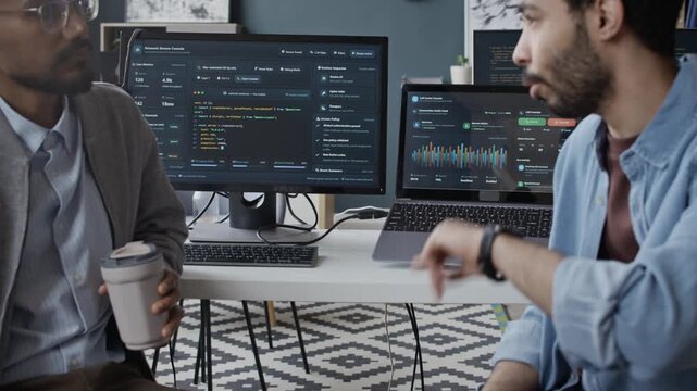 Handheld shot of Middle Eastern and Indian young male colleagues discussing data analytics during coffee break in office. For tech startup marketing and corporate software development
