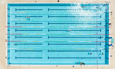 Obraz premium Aerial top down view of a bright blue swimming pool divided into multiple lanes having colorful floating markers, showing several athletes training together during a sunny summer day. Zenithal shot.