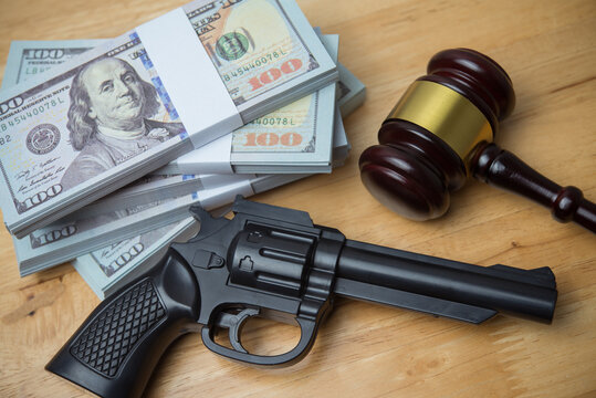 Judge gavel, a handgun and US dollar bill banknotes on wooden table background in courtroom. Crime and punishment, illegal, law, justice, corruption, dirty money, money laundering and so on concept.