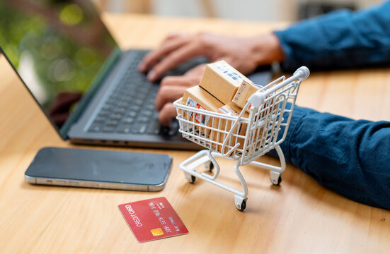 Close up hands of business man type the keyboard of laptop on table with mobile phone, credit card and cart with small box inside are in front of the man 