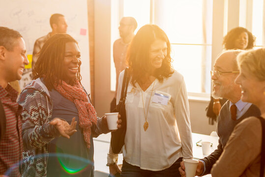 Diverse group of people socializing at a sunlit event, smiling warmly.