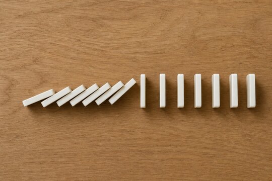 A line of falling dominoes halted by one turned piece, overhead view on wood.
